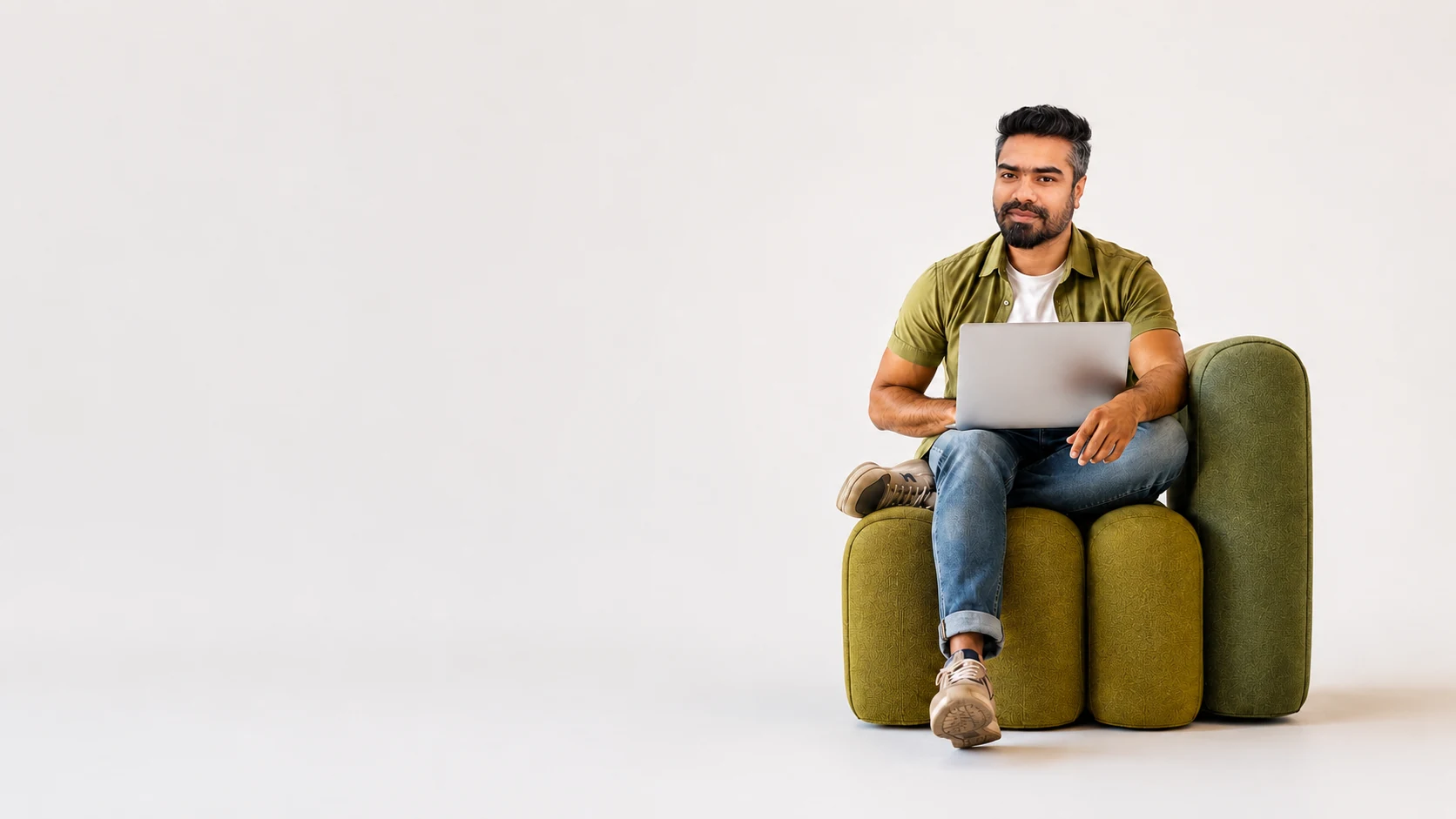 Hasan Syed, web designer and developer, working on a laptop while seated in a modern green armchair
